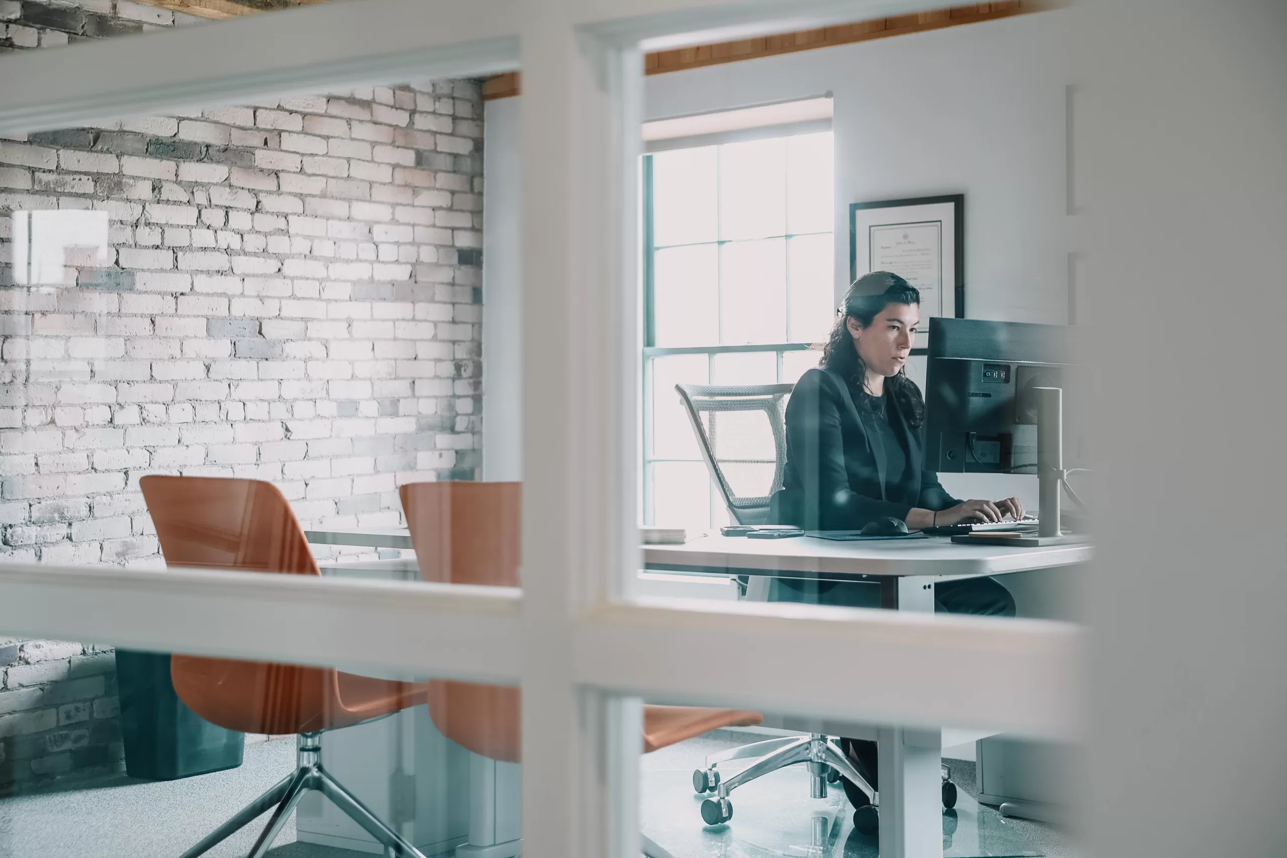 Woman working at computer in modern office with brick wall.
