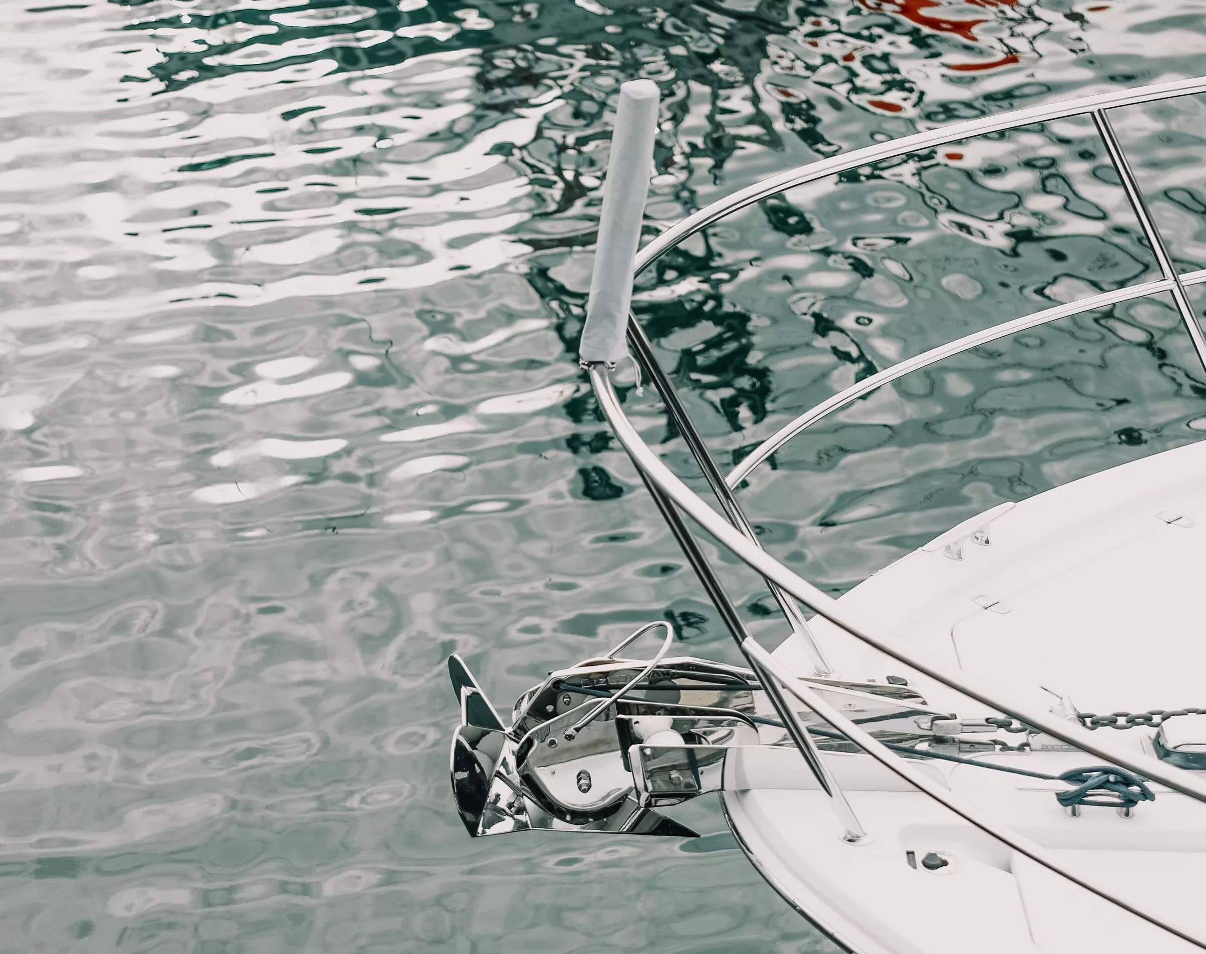 Front part of a white boat showing anchor and railing on rippled water.